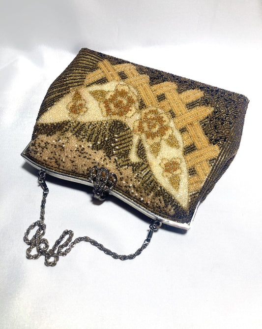 May include: Vintage beaded handbag with a silver-tone frame and chain strap. The bag features a floral design in shades of gold, cream, and brown. The intricate beadwork creates a textured surface, adding to its vintage charm. The clasp is ornate.