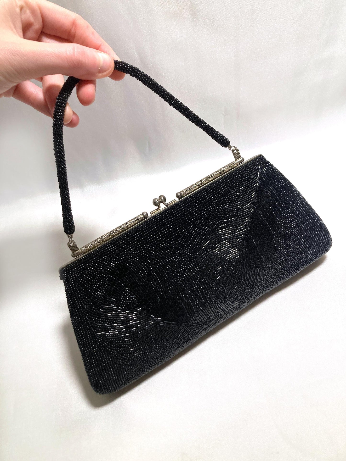 May include: Black beaded evening bag with a beaded handle and silver-tone clasp. The rectangular clutch features a floral design and is approximately 10 inches wide.