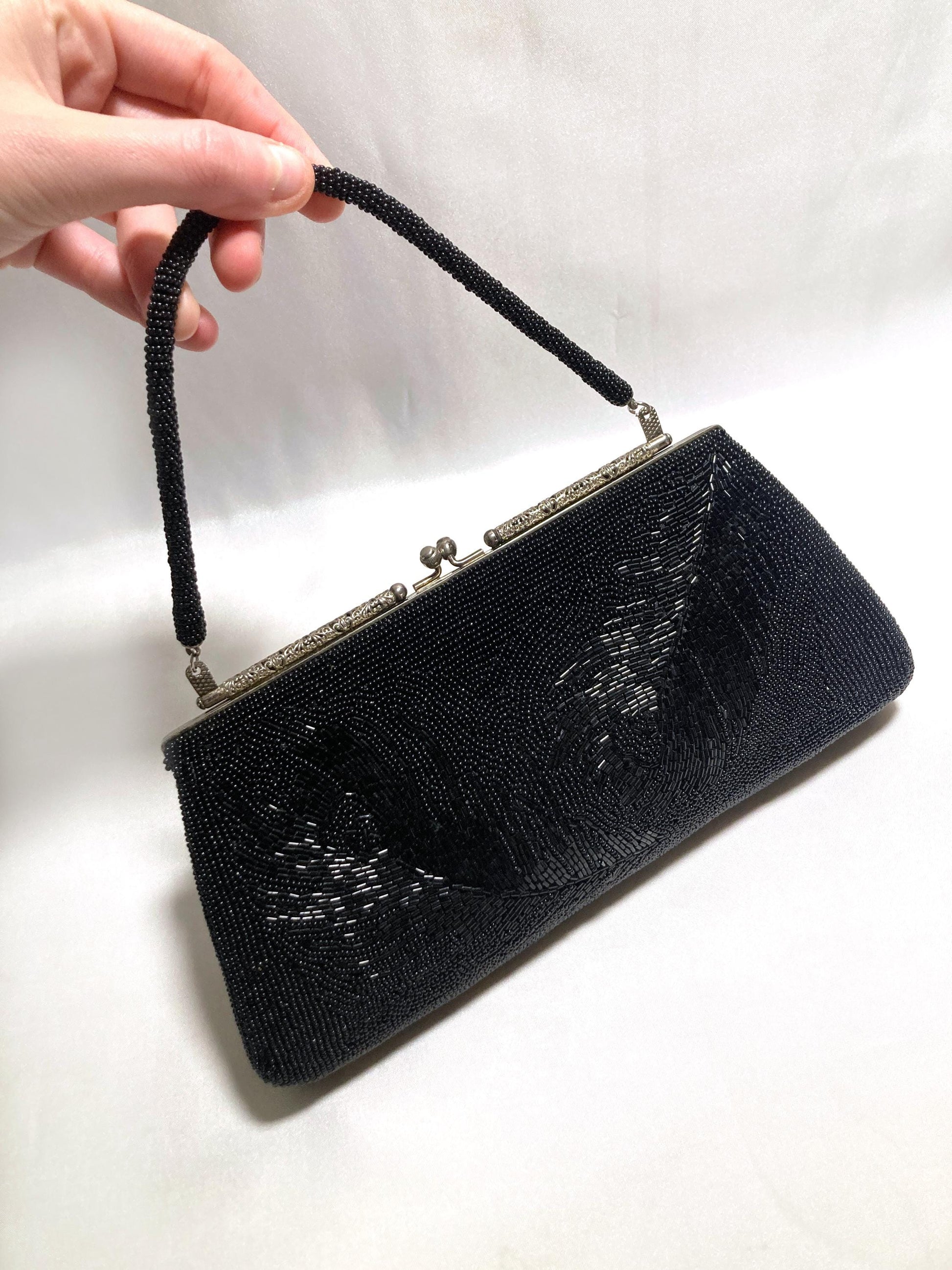 May include: Black beaded evening bag with a beaded handle and silver-tone clasp. The rectangular clutch features a floral design and is approximately 10 inches wide.