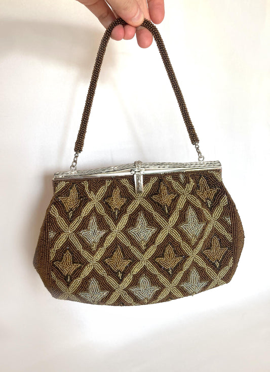 May include: A vintage beaded handbag with a silver clasp and handle. The bag features a geometric pattern of brown, gold, and silver beads. The handle is made of brown beads. The bag is held up by a hand.