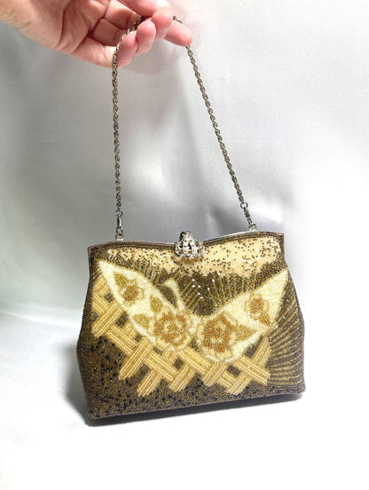 May include: Vintage beaded handbag with a silver chain strap. The bag features a butterfly design in gold and cream beads on a dark brown background. The clasp is silver with a decorative jewel.