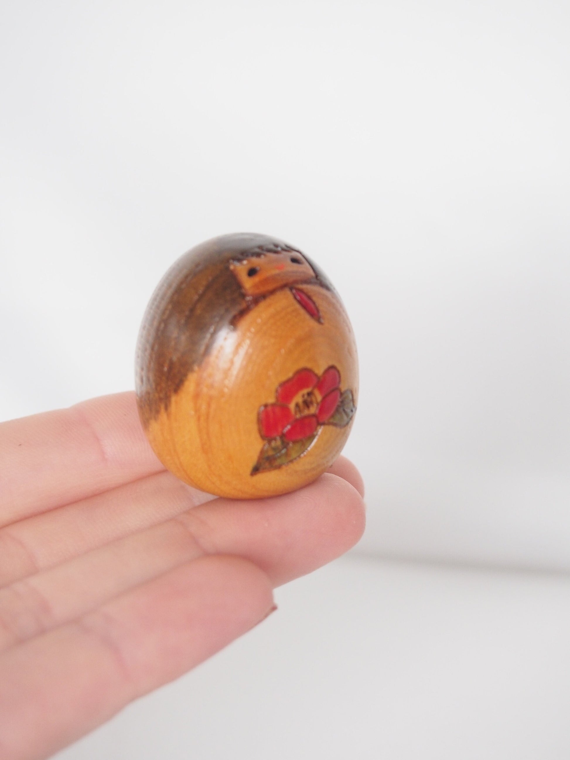 Miniature wooden kokeshi doll with a camellia flower