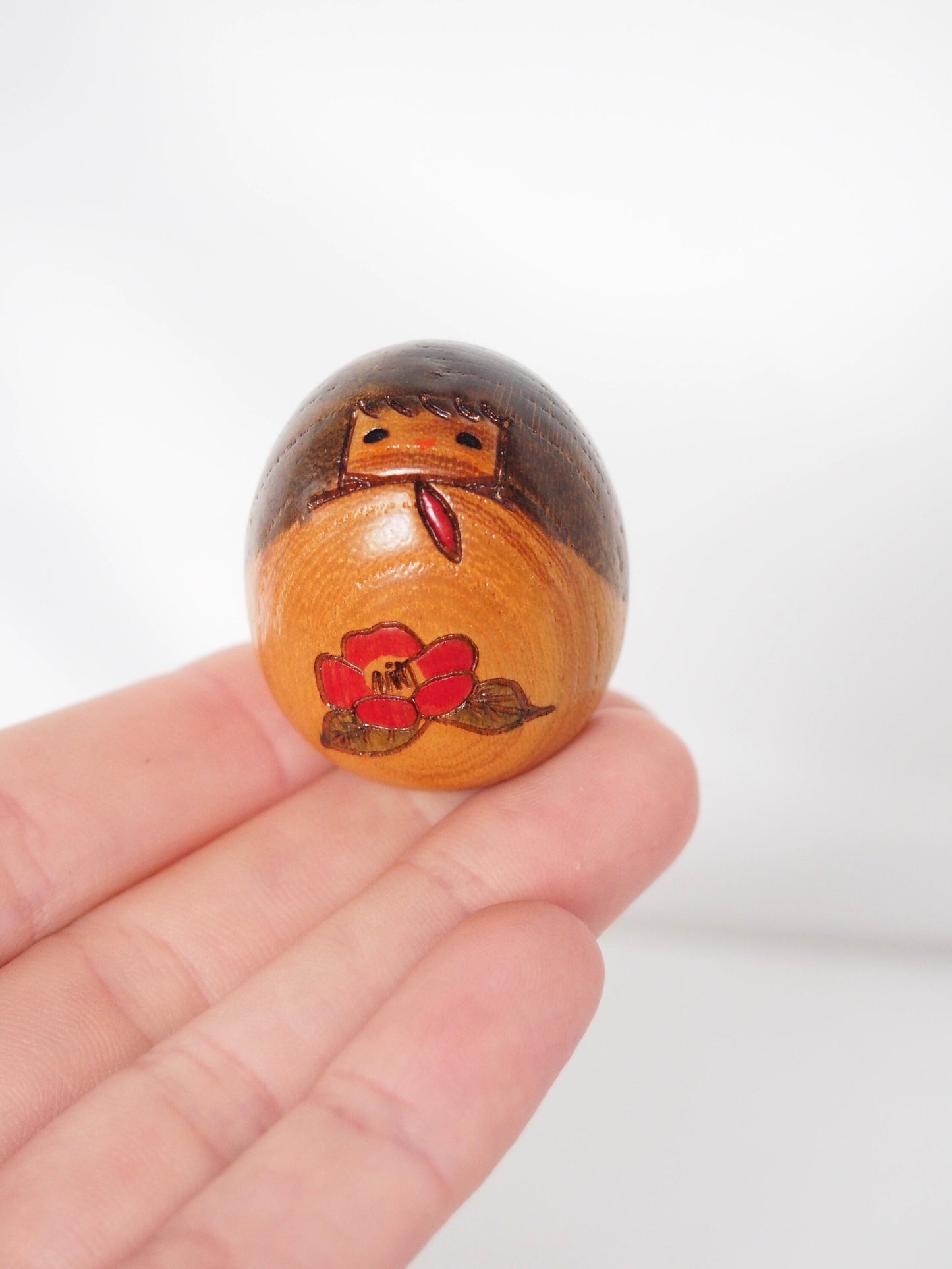 Miniature wooden kokeshi doll with a camellia flower