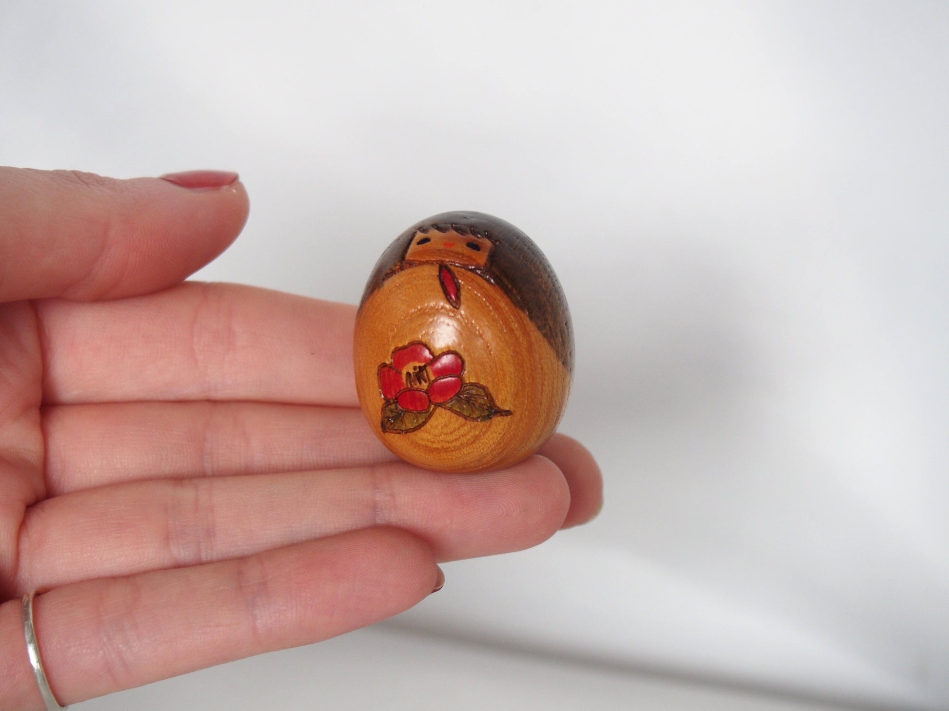 Miniature wooden kokeshi doll with a camellia flower
